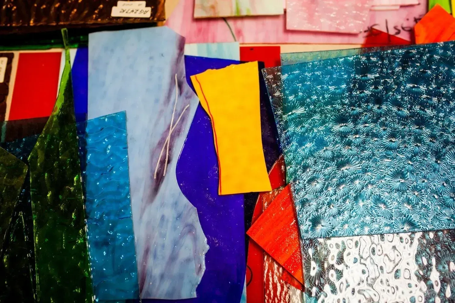 Assorted colorful stained glass sheets, including blue, green, yellow, and red, arranged close together.