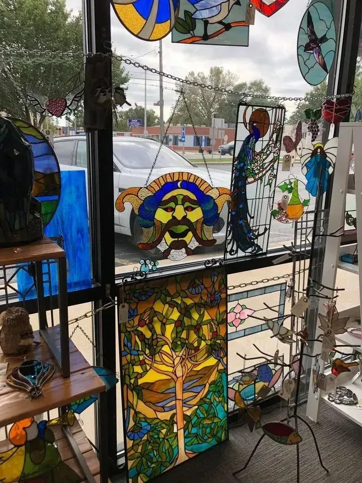 Stained glass art in a shop window, including a face, tree, and other colorful designs.
