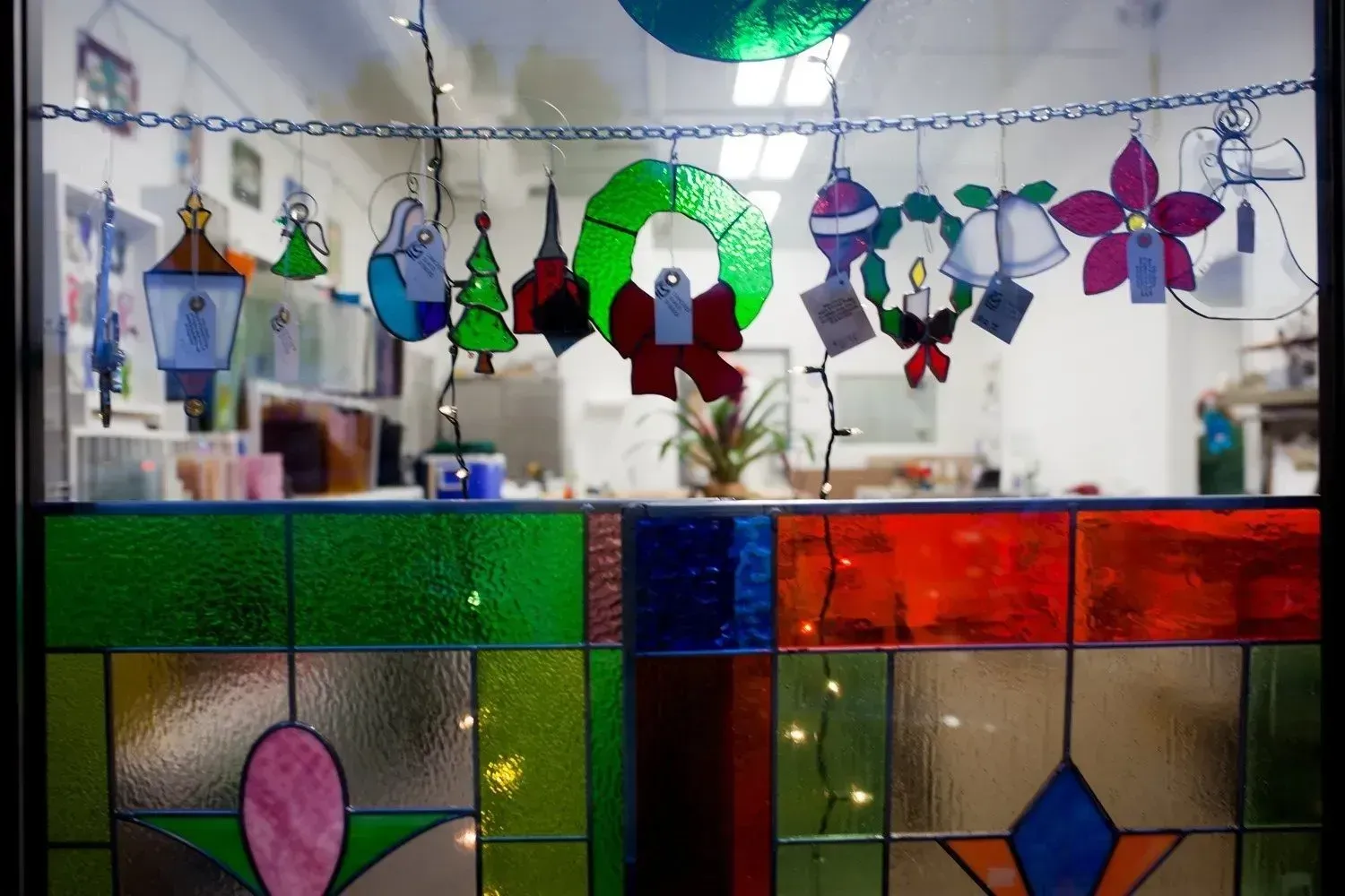 A colorful window with stained glass and hanging Christmas decorations inside a building.