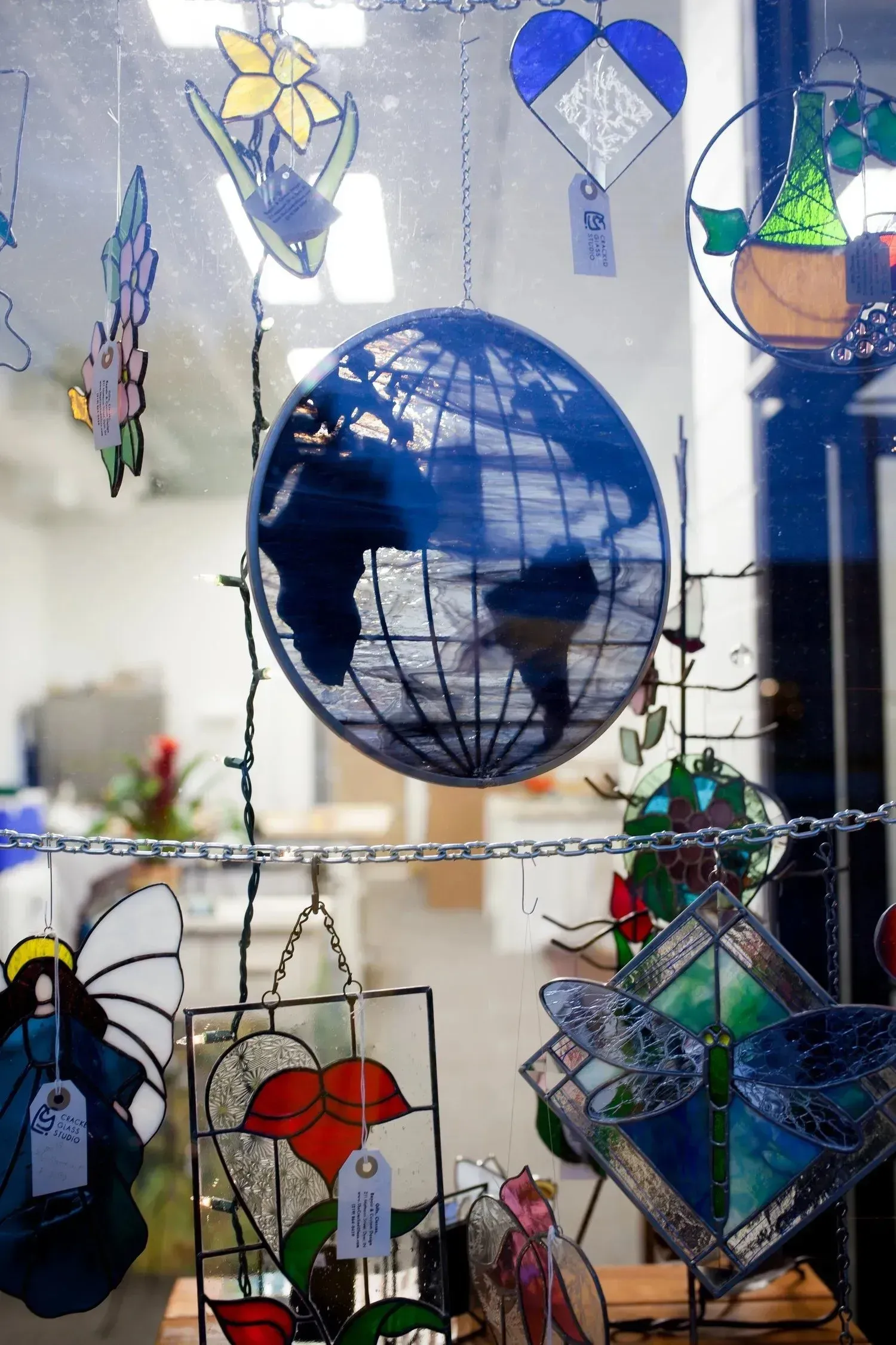 Stained glass globe and other colorful shapes hang in a window display, including flowers, angels, and hearts.