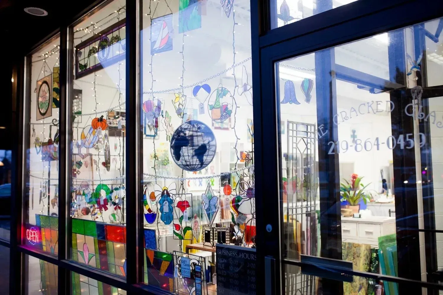 Shop window display: colorful artwork, hanging decorations, and a globe. Glass door with reflection of a street.
