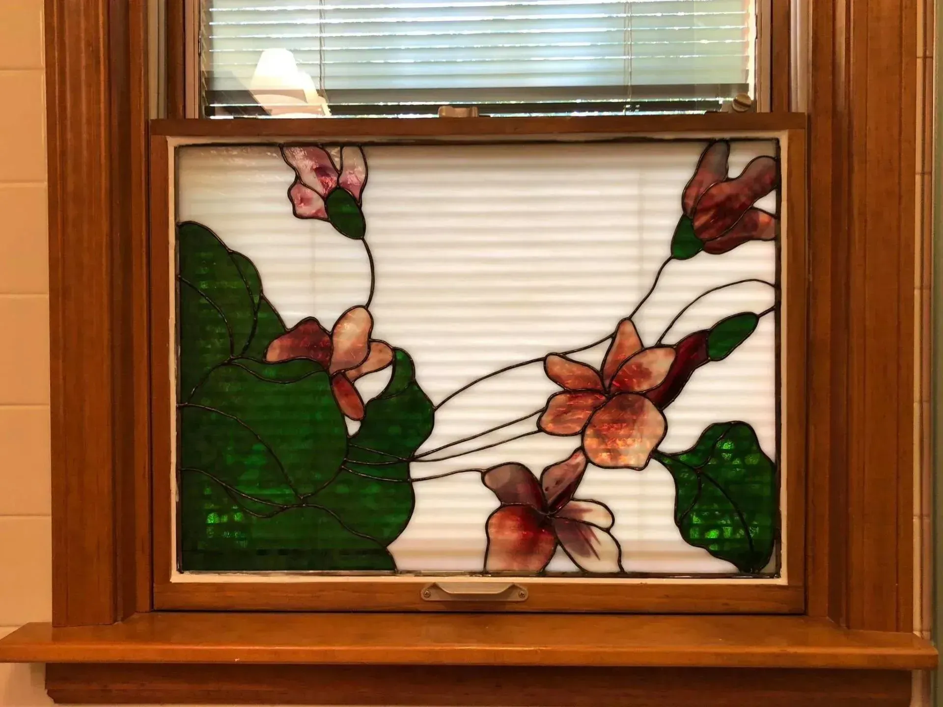 Stained glass window with pink flowers, green leaves, and white background, set in a wooden frame.