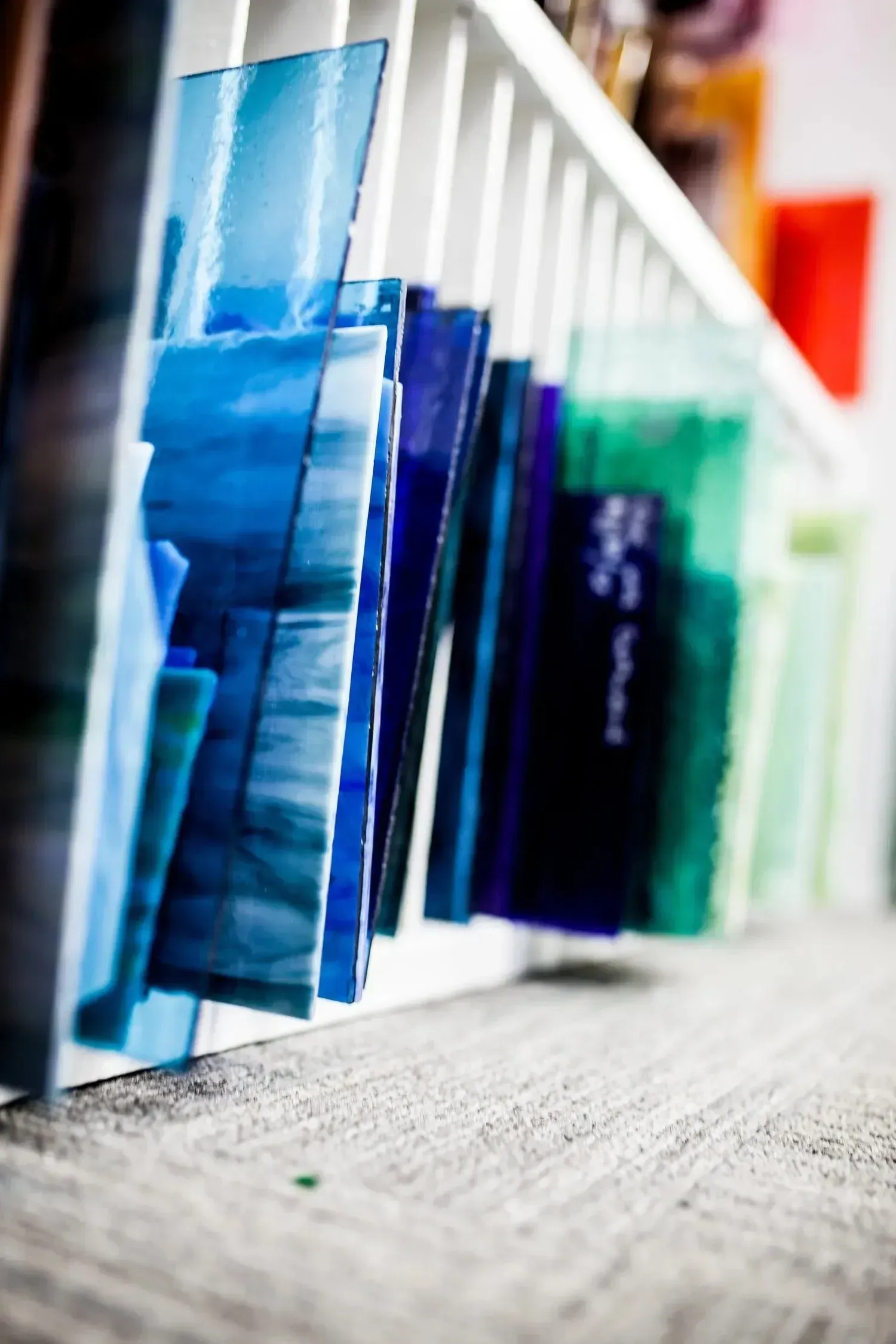 Stacks of blue and green glass sheets, stored in a white slotted shelf.