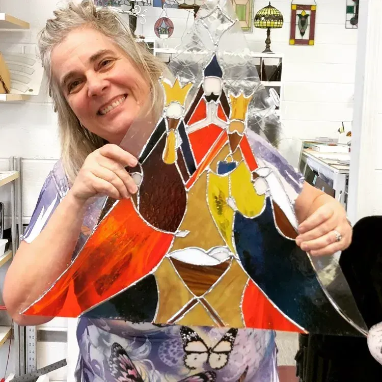 Woman holding stained glass depicting the three wise men; smiling, art studio backdrop.