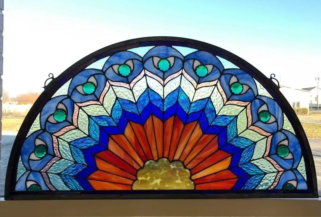 Stained glass window, semicircle shape. Blue, orange, and green peacock feather design.