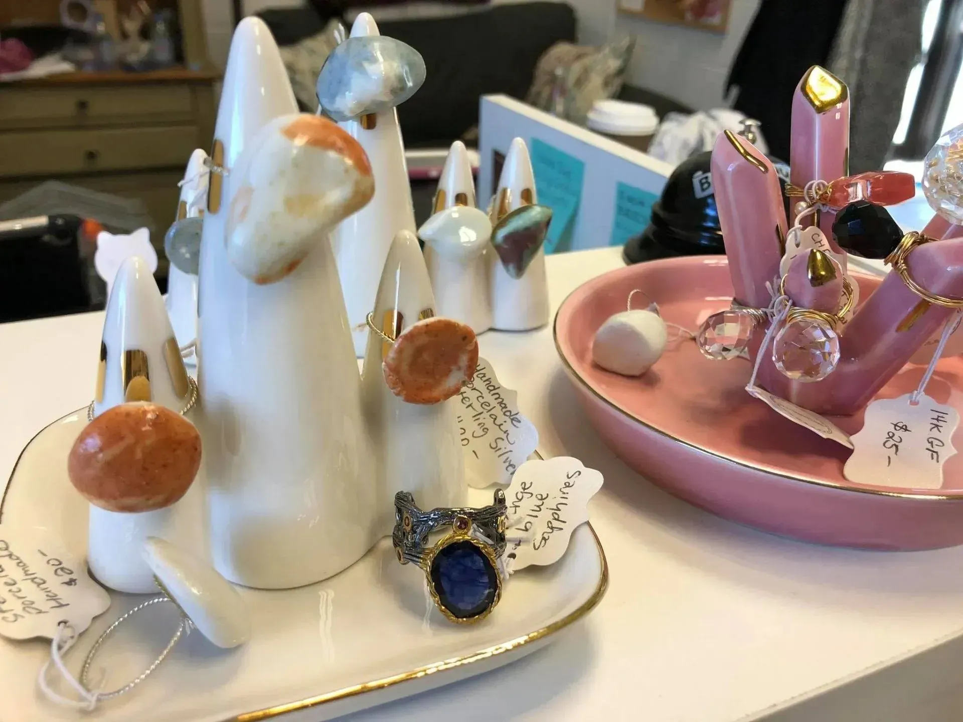Jewelry display with white ceramic ring holders and pink dish. Rings with various stones on display.
