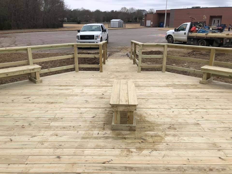 A wooden deck with benches and a truck parked in the background.