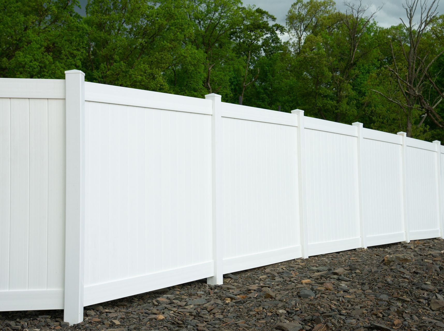 A white vinyl fence is sitting on top of a pile of rocks.