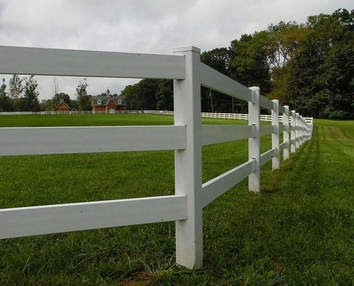 A white fence surrounds a grassy field with a house in the background