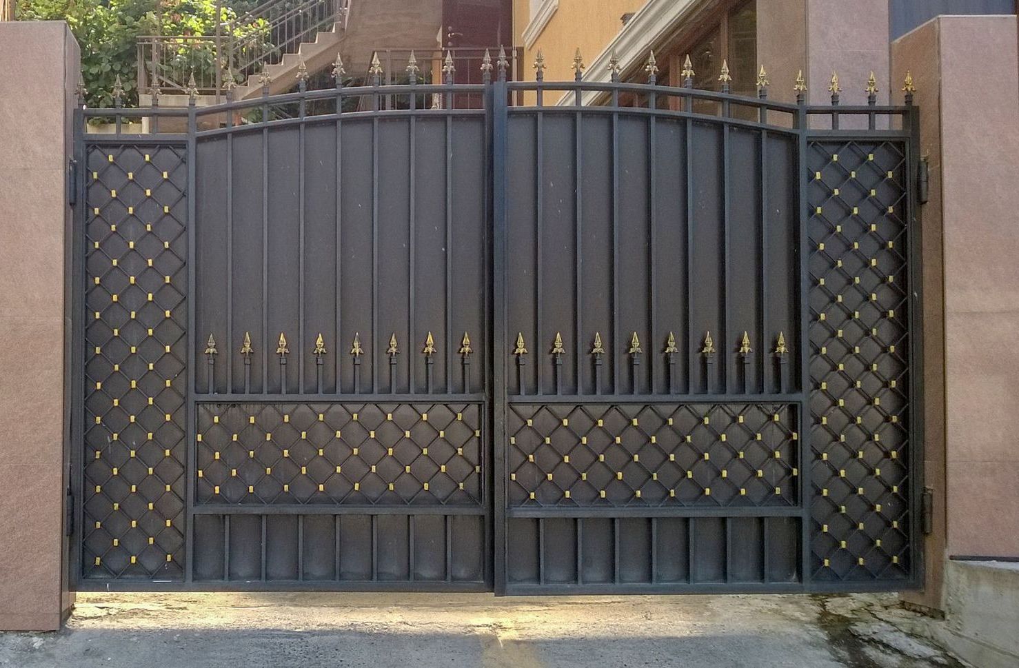 A wrought iron gate is open to a driveway in front of a building