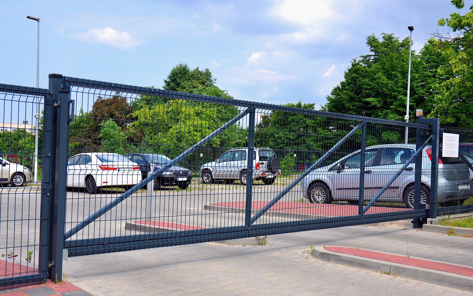 Cars are parked in a parking lot behind a sliding gate.