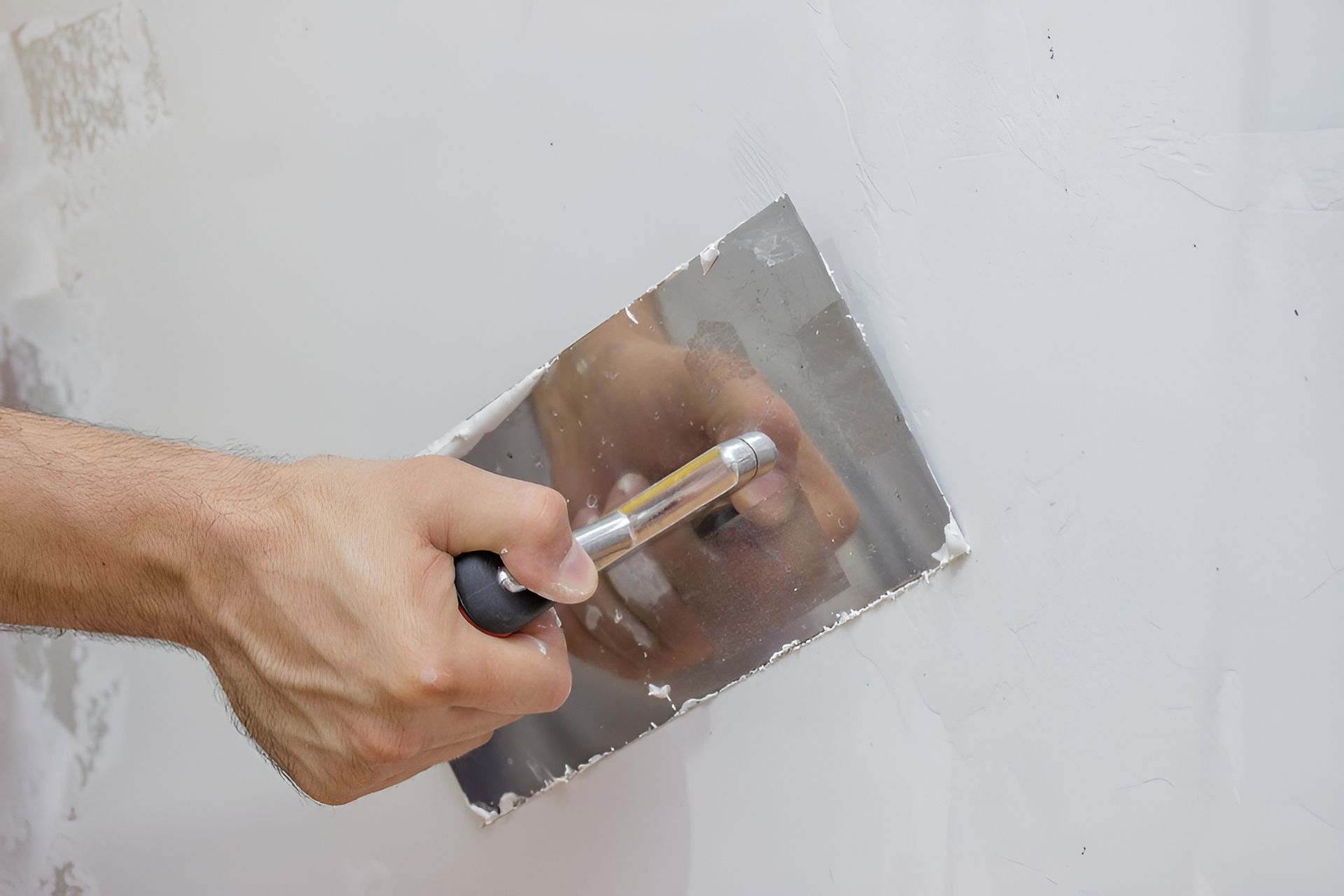 Hand Using a Putty Knife to Smooth White Wall Compound — Frenchy’s Plaster & Paint in Bellamack, NT