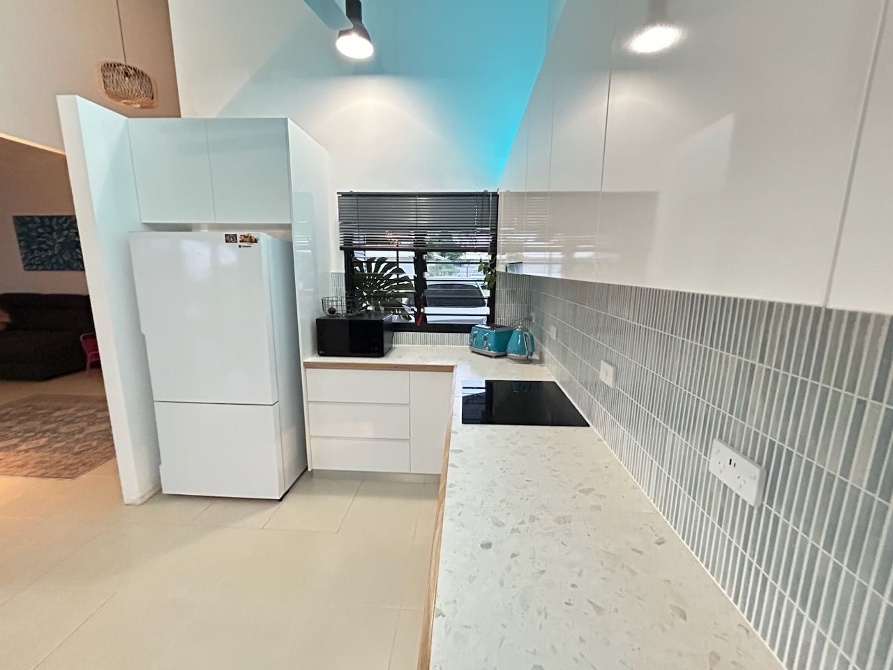 A modern kitchen with white cabinetry, quartz countertops, a white refrigerator, and gray vertical tiled backsplash.