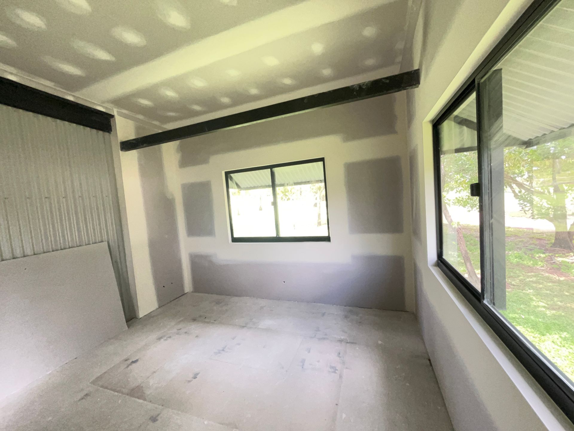 An unfinished room with bare drywall, a large window, and a dark support beam across the ceiling. — Frenchy’s Plaster & Paint in Bellamack, NT