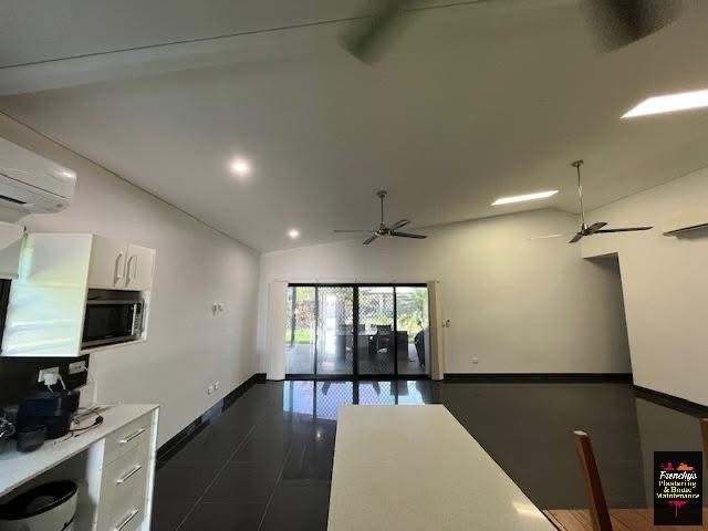 A modern open-plan living area with white walls, dark flooring, a kitchen counter, and glass sliding doors to a patio. — Frenchy’s Plaster & Paint in Bellamack, NT