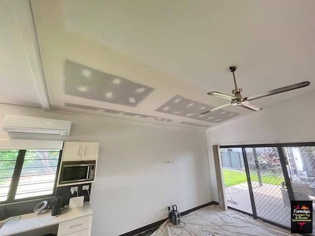 A modern interior room with a ceiling fan, white walls, built-in kitchen cabinetry, and large windows looking outdoors. — Frenchy’s Plaster & Paint in Palmerston, NT