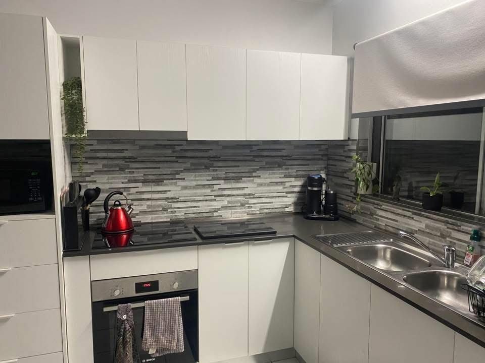 A modern kitchen with white cabinets, a dark countertop, a stacked stone backsplash, and stainless steel appliances. — Frenchy’s Plaster & Paint in Bellamack, NT