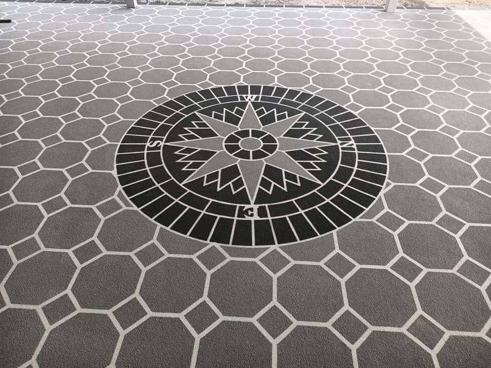 A compass rose design in the center of a gray tiled surface. Geometric pattern surrounds it.