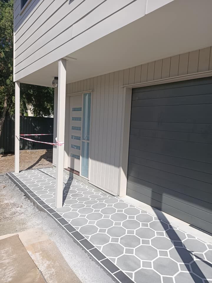Two-story house with gray door and garage, light gray siding, and patterned gray and white tiled walkway.