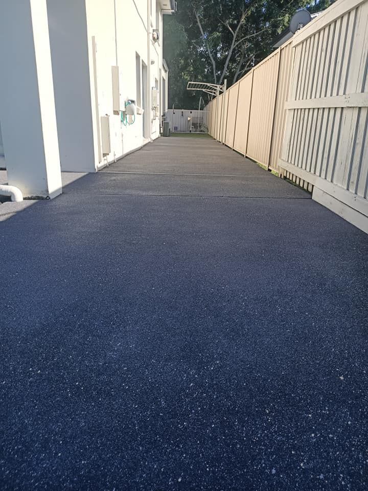 Dark asphalt walkway between a white building and a light fence.