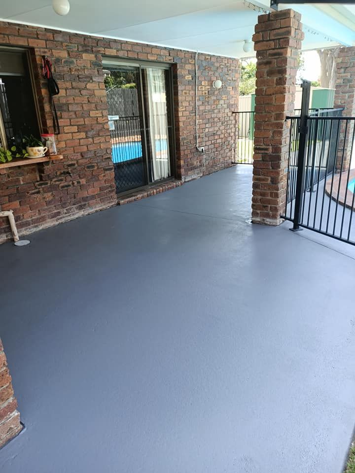 A paved patio with a smooth gray floor, brick walls, and a black metal fence beside a pool.