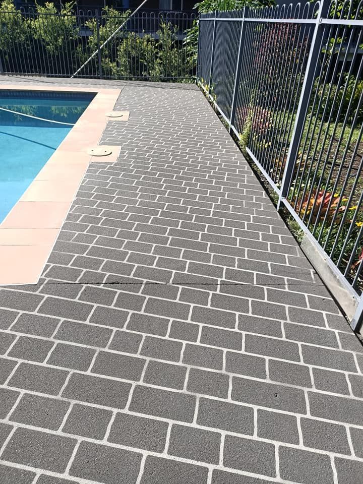 Brick-patterned pool deck alongside a swimming pool and black metal fence.