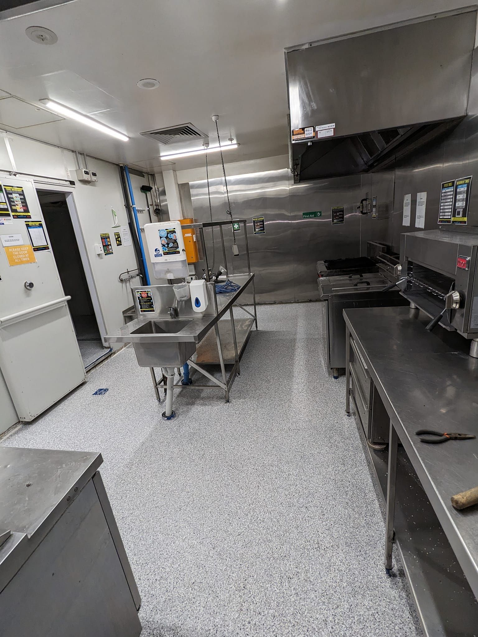 Commercial kitchen with stainless steel appliances and speckled floor.
