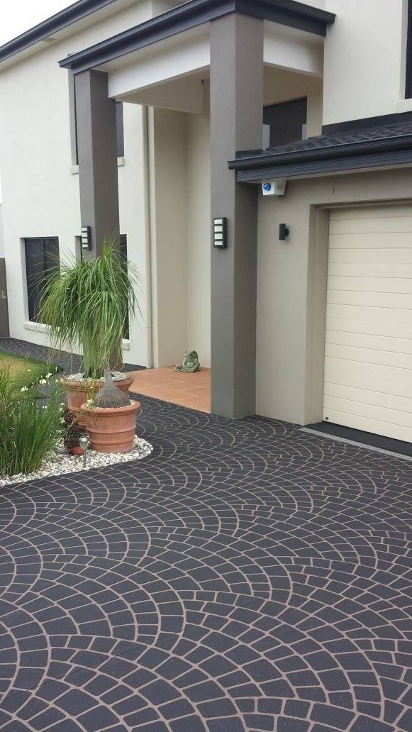 Driveway of a modern home with black paving stones. Planted flowerbeds flank the walkway to the entrance.