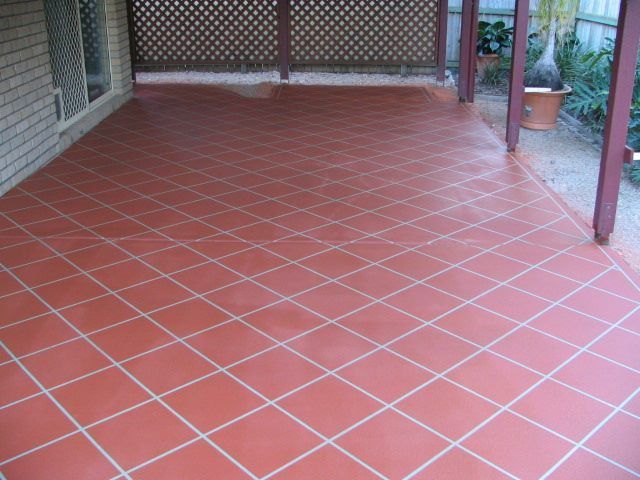 Brown concrete driveway with caution tape, leading to a house with a tan garage door and green roof.