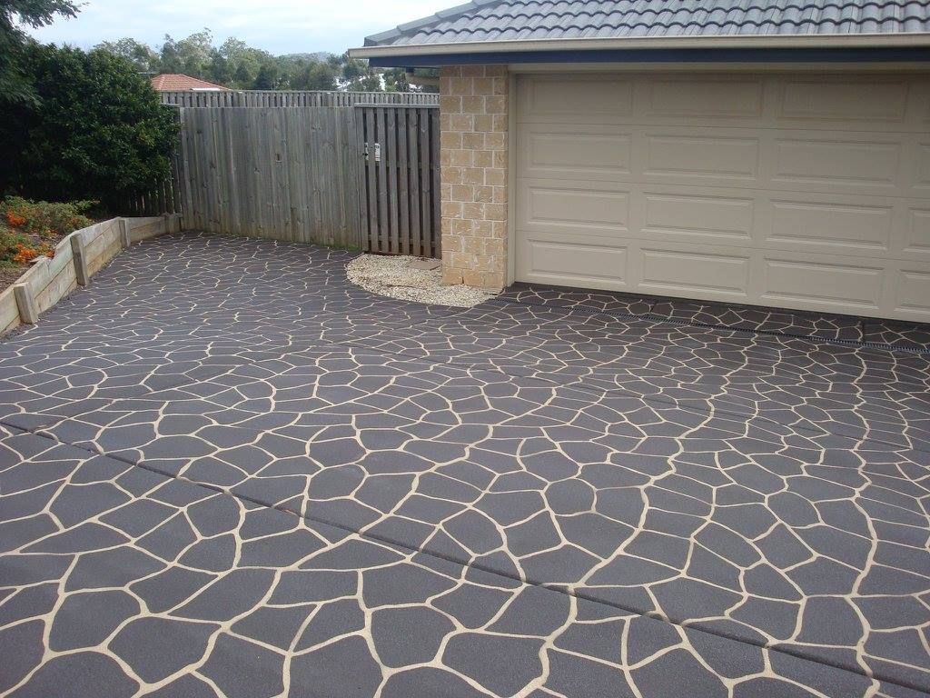 Driveway with dark patterned concrete leading to a garage. A wooden fence and vegetation are in the background.