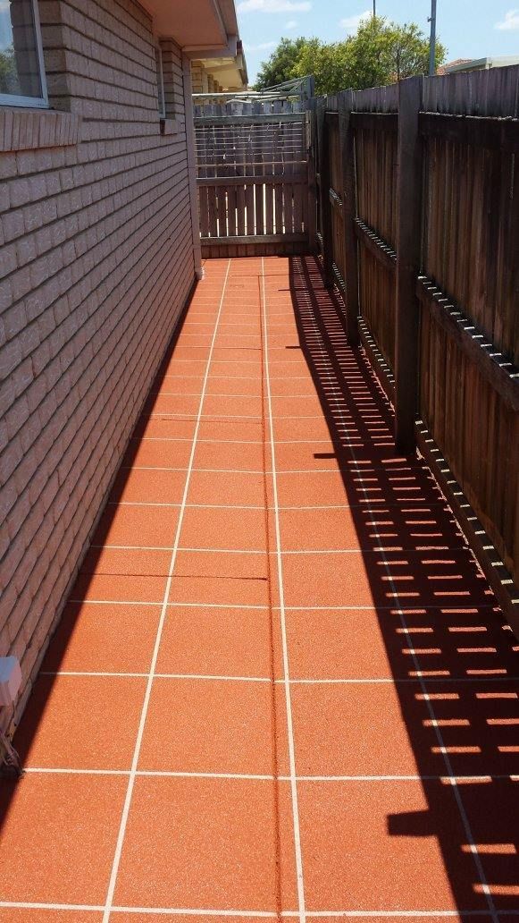 Long, narrow brick pathway between a brick wall and a wooden fence, leading to a gate.