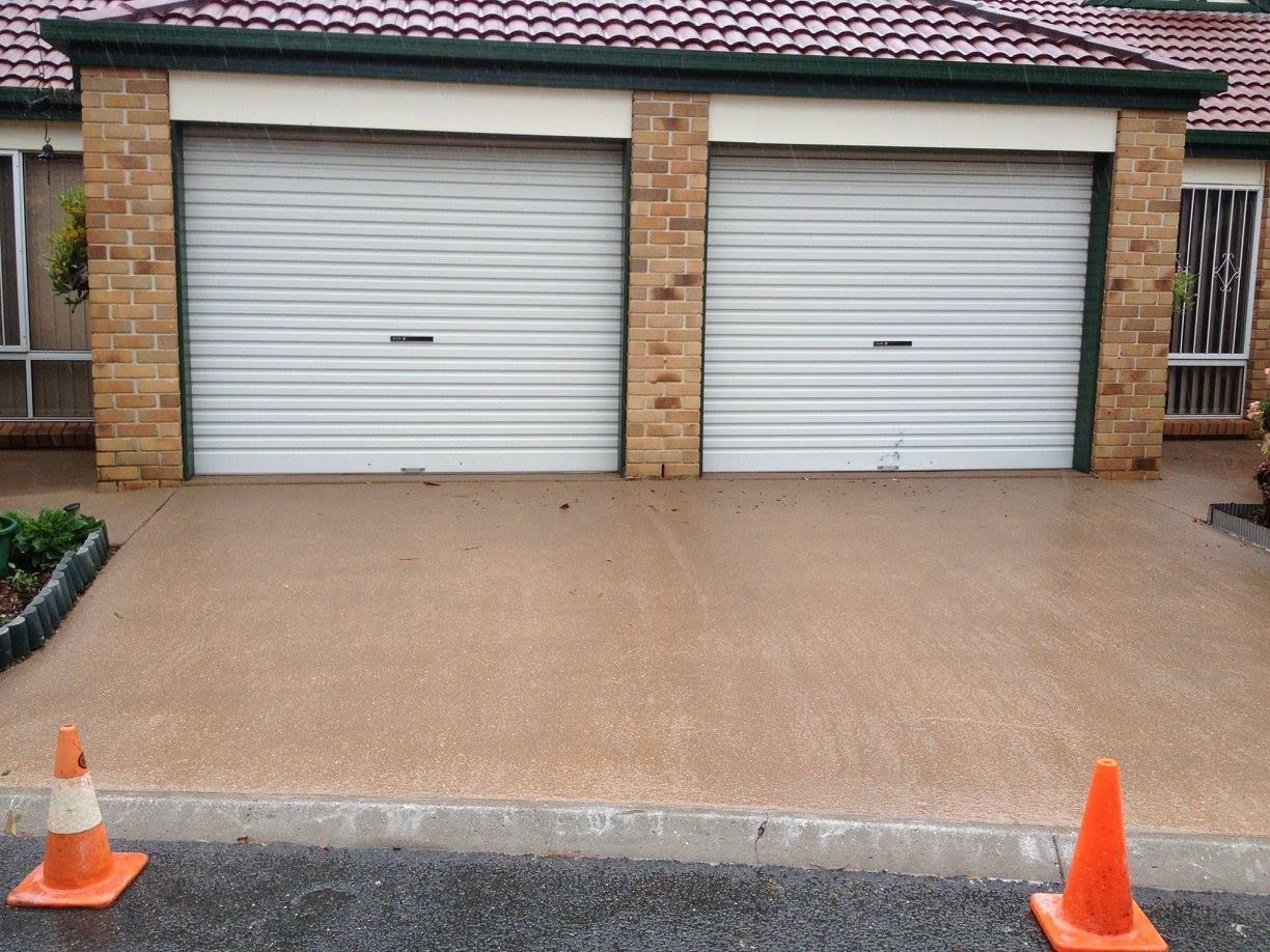 Two white garage doors in brick structure, with tan driveway and two orange traffic cones.