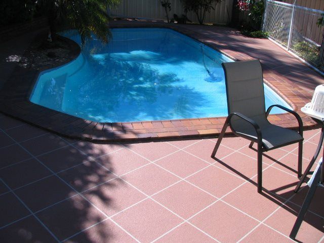 Swimming pool with blue water and red tiled patio, with a chair.
