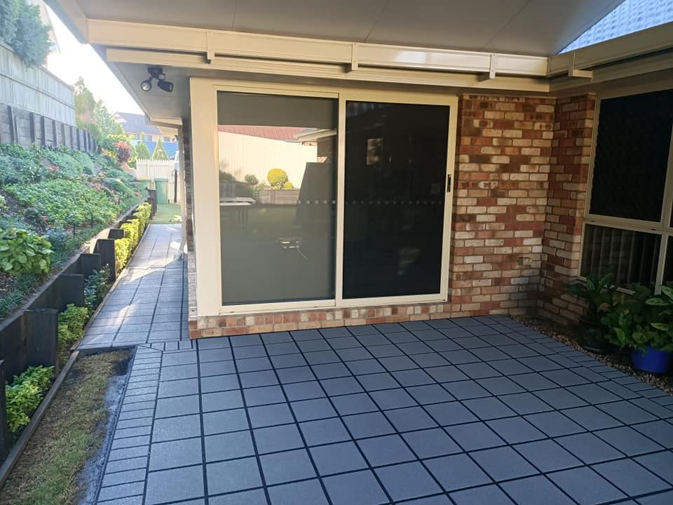 Patio with gray tiled floor, brick wall, sliding door, and garden bed.