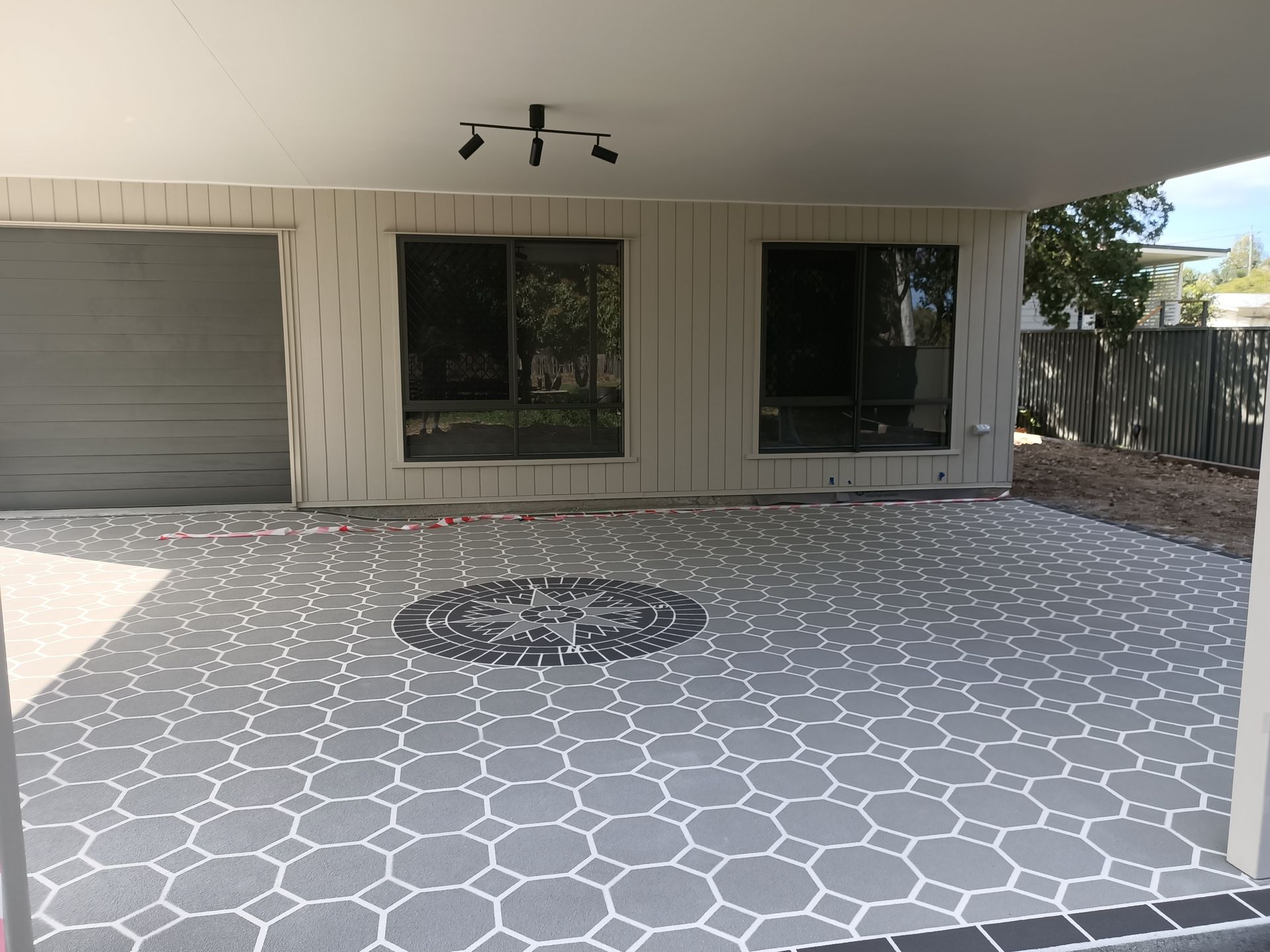 Covered patio with gray and white patterned floor, black accent circle, and garage door.