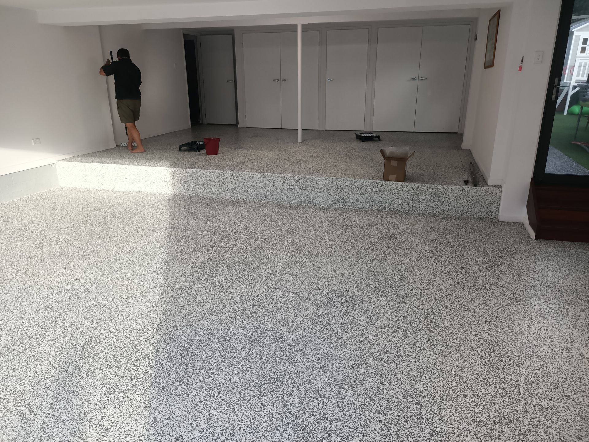 A room with a shiny, light-gray epoxy floor; stairs to the right, kitchen in the background.