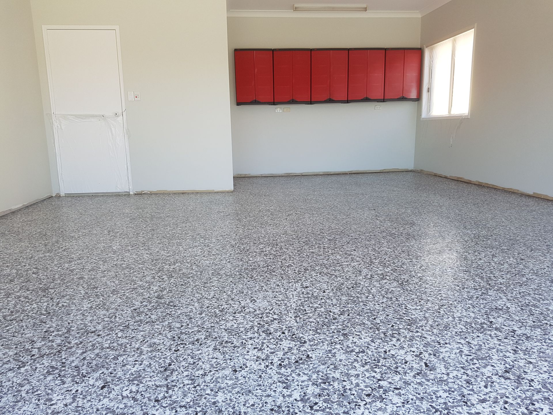 Man painting a white wall in a basement with a speckled, light gray floor.