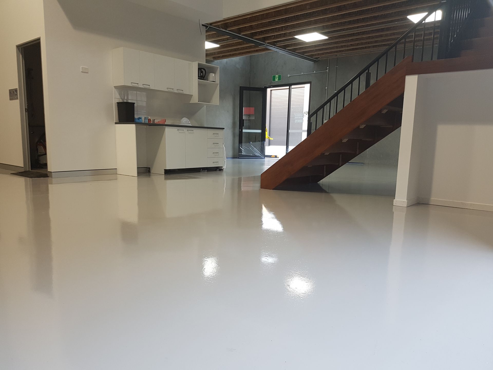 Empty room with gray concrete floor, white lines, beige walls, and overhead lights.
