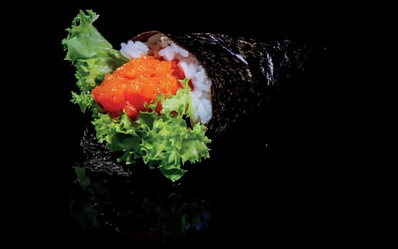 Primo piano di un rotolo di sushi con lattuga e caviale su sfondo nero.
