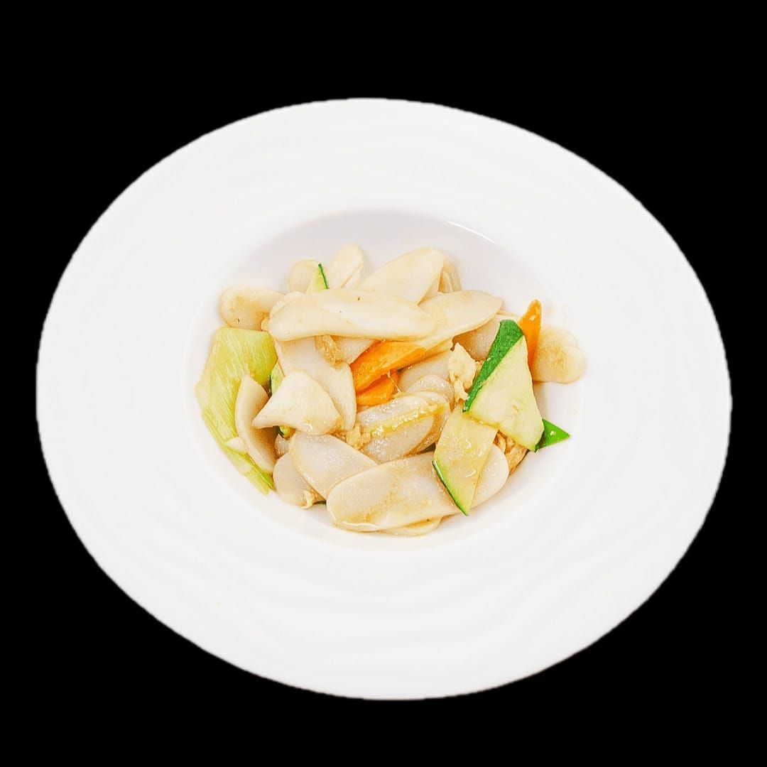 Un piatto bianco con sopra noodles e verdure su uno sfondo nero.