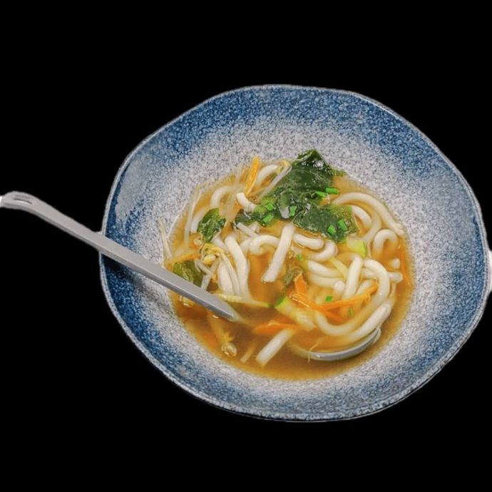 Una ciotola di noodles e verdure con un cucchiaio dentro.