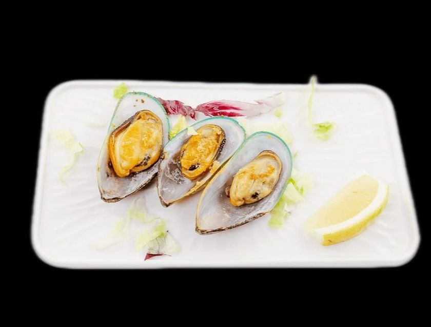 Un piatto bianco con sopra delle cozze e una fetta di limone.