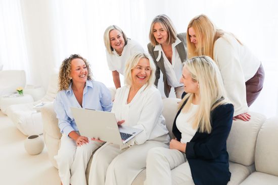 Pam Shanker in a white shirt is smiling with her hand on her face