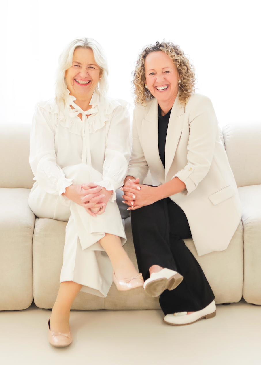 Two women are standing next to each other in front of a sign.