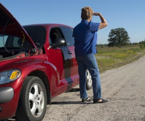 Woman by red car with open hood on rural road, looking away.