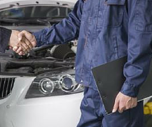 Mechanic shaking hands with a customer by a car with an open hood; car repair.