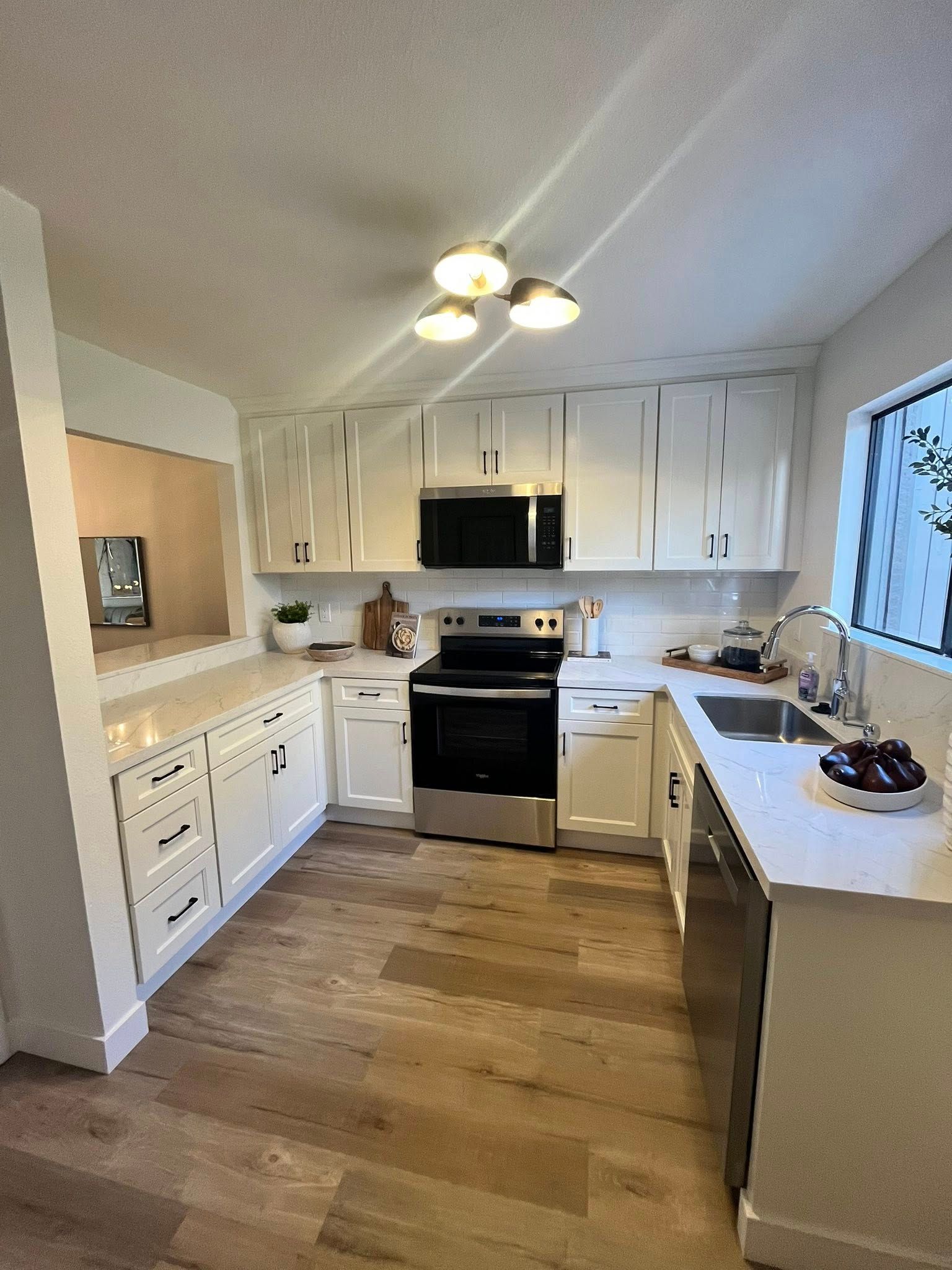 A kitchen with white cabinets , stainless steel appliances , a sink , and a window.