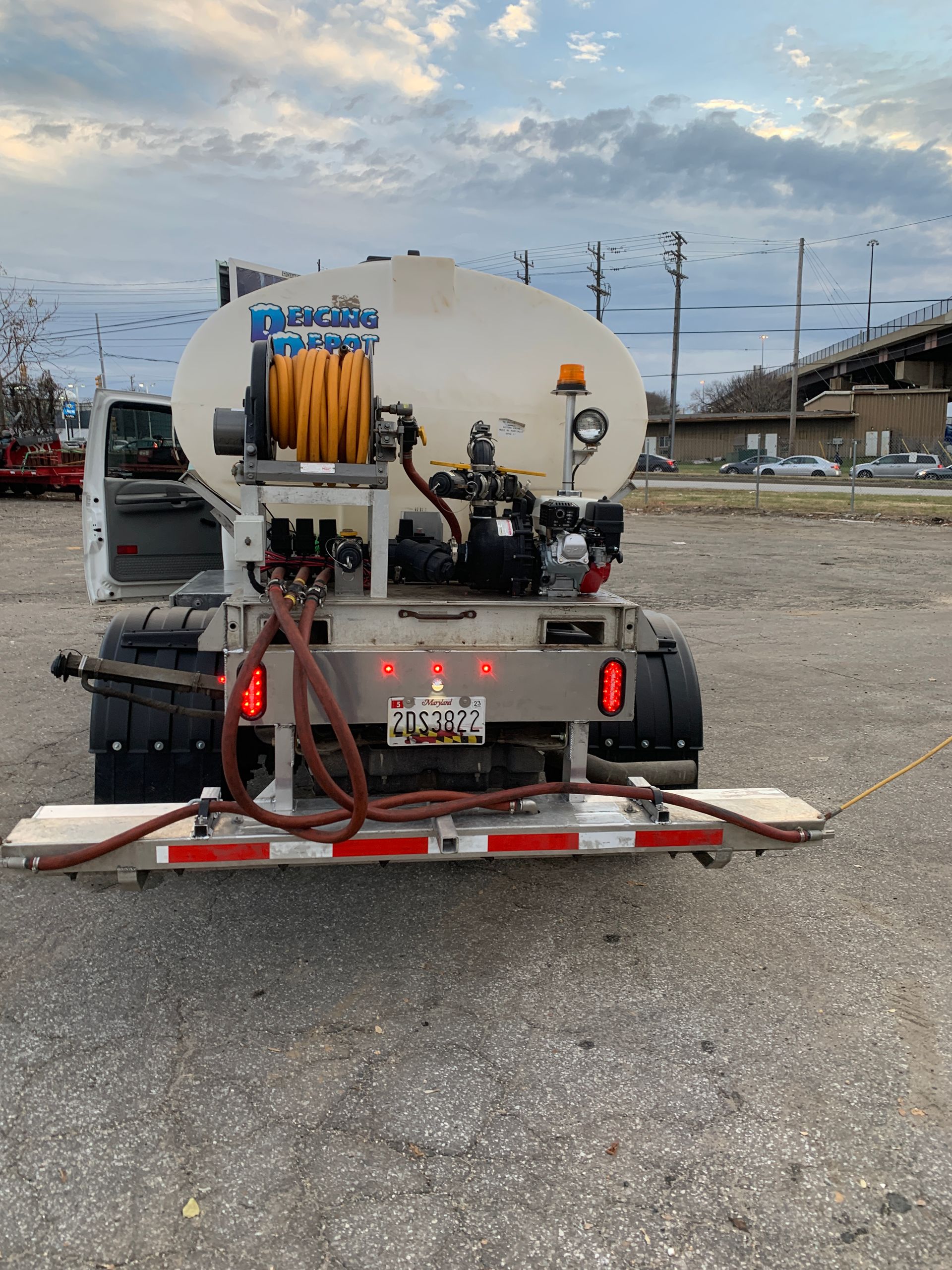 A white truck with a hose attached to the back is parked in a parking lot.