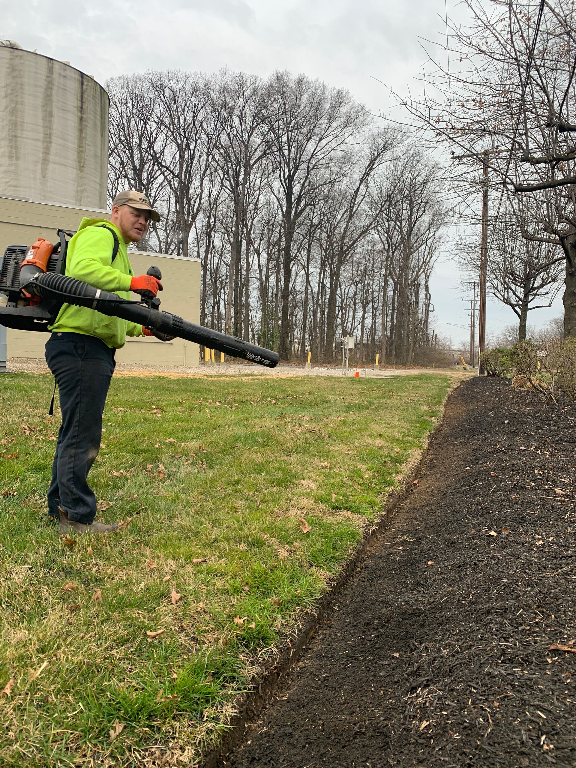 A man is blowing leaves in a field with a backpack blower.