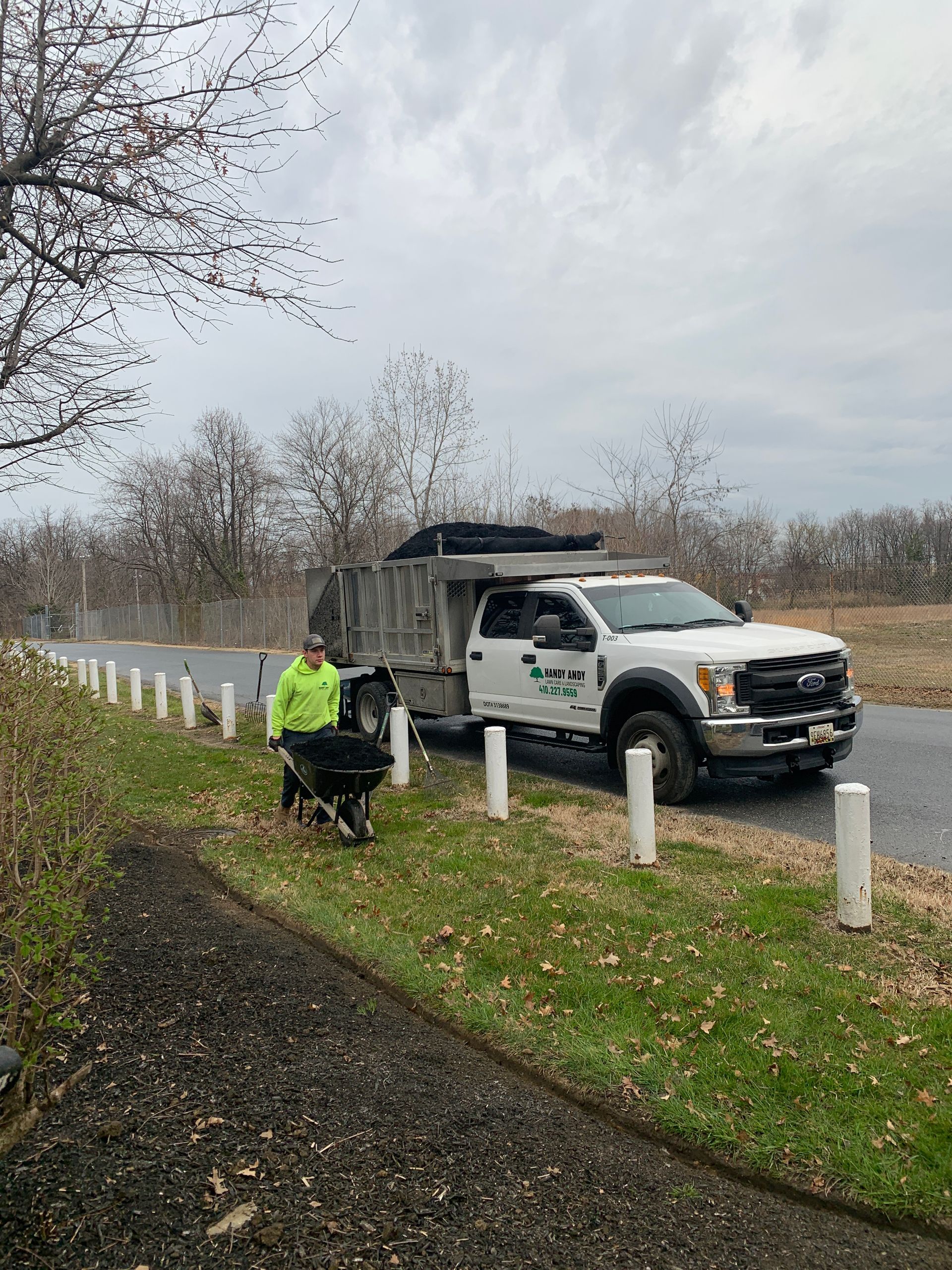 A man is pushing a wheelbarrow next to a dump truck.